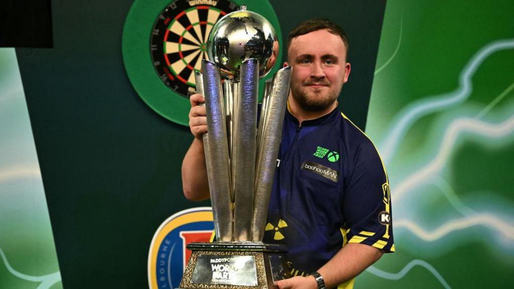 Luke Littler holding the World Darts Championship trophy