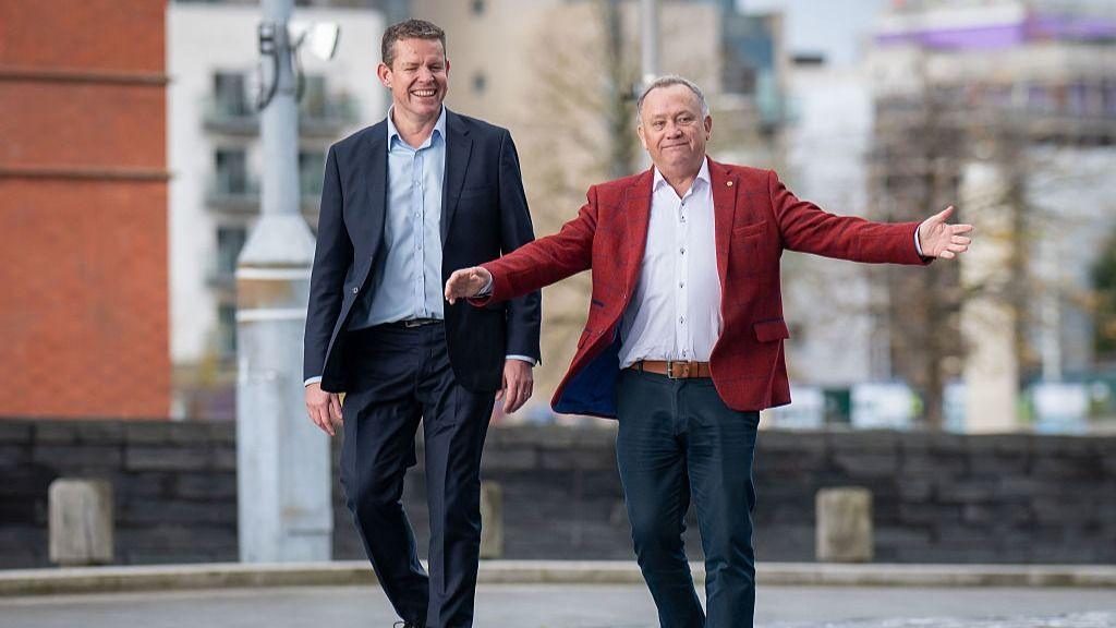 Newly-elected Senedd Member for Caerphilly Lindsay Whittle, dressed in a scarlet jacket, arrives at the Senedd in Cardiff Bay, with a smiling Plaid Cymru leader Rhun ap Iorwerth, on the steps of the building.
