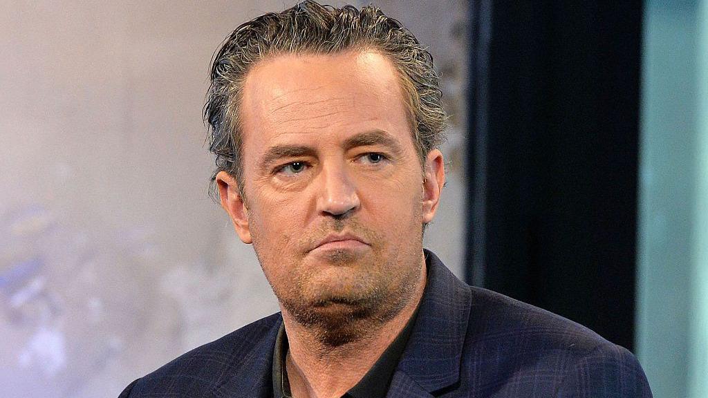 Matthew Perry is seen wearing a suit jacket. His hair is slightly slicked back