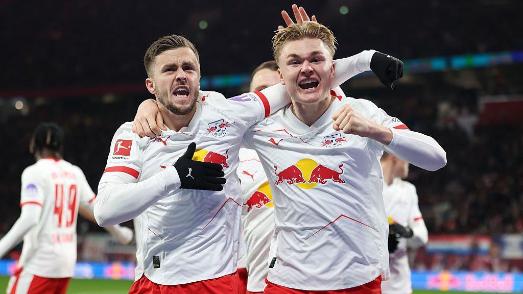 Conrad Harder celebrates RB Leipzig's opening goal against Eintracht Frankfurt with Christoph Baumgartner who provided the assist. Both players are wearing white shirts with red shorts.
