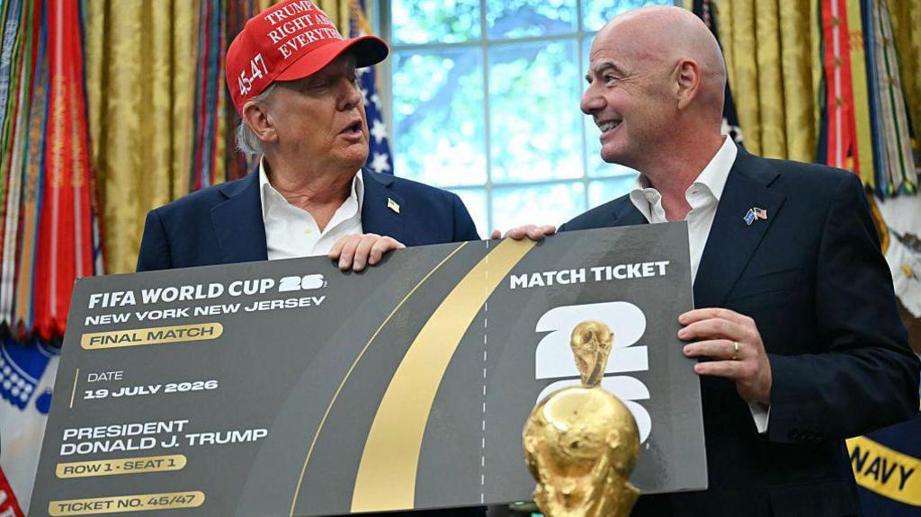 Donald Trump and Gianni Infantino are stood together in The Oval Office holding an oversized World Cup final ticket.