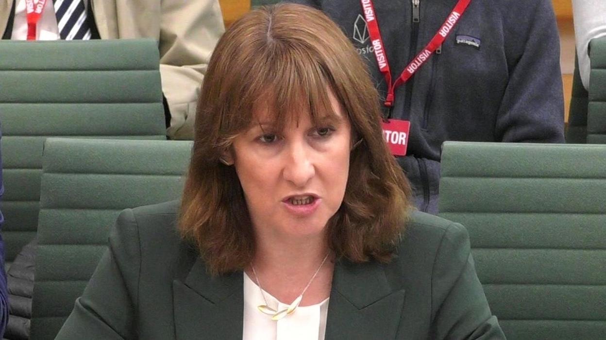 Rachel Reeves giving evidence to the Treasury select committee. She wears a sage green jacket, a white top and a silver necklace with three silver leaves.