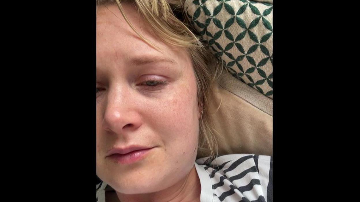Blonde woman with striped T-shirt looking unwell and tired.
