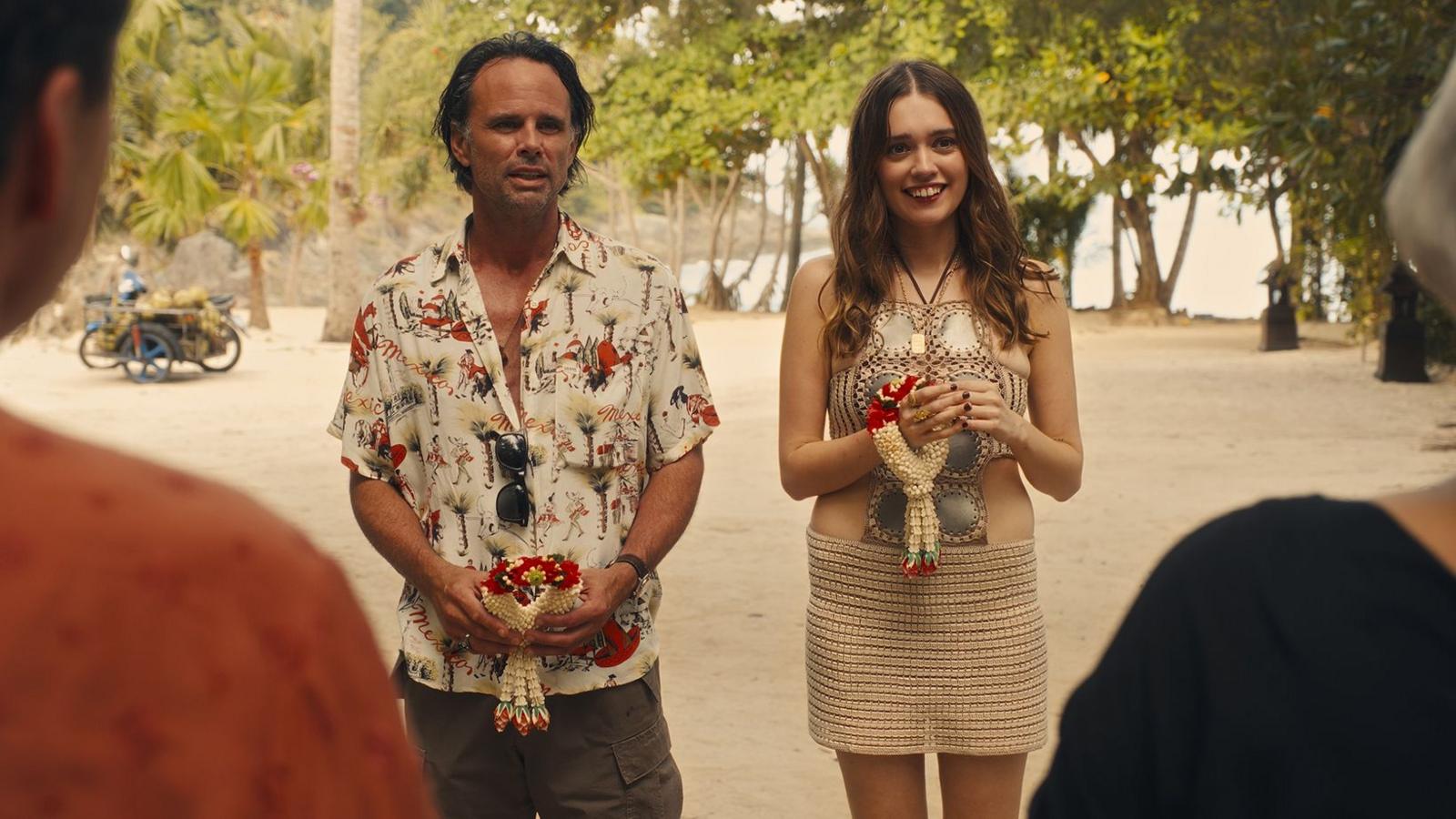 Walton Goggins and Aimee Lou Wood, in costume, stand next to each other on a beach in a scene from The White Lotus