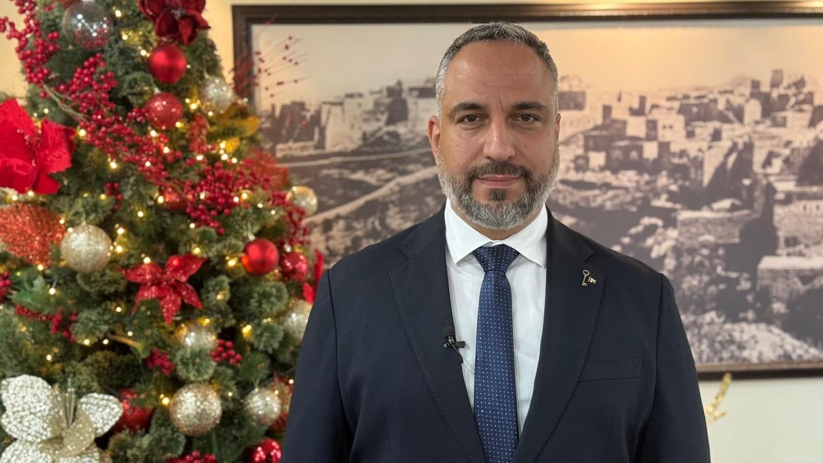 Bethlehem's mayor Maher Canawati stands next to a Christmas tree with red and gold decorations