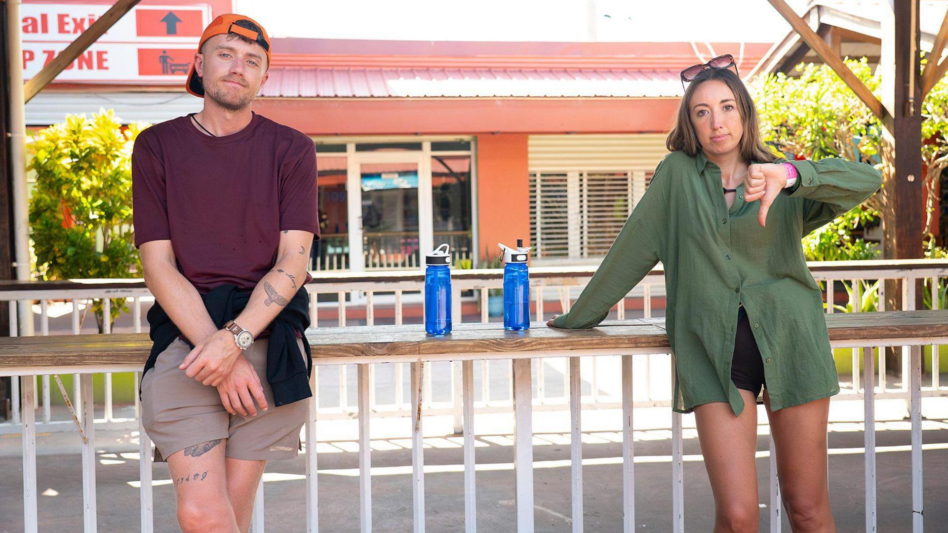 Broadcaster Roman Kemp and his sister, singer-songwriter, Harleymoon leaning against a wall whilst waiting for transport. Harleymoon signals a thumbs down with her hand.
