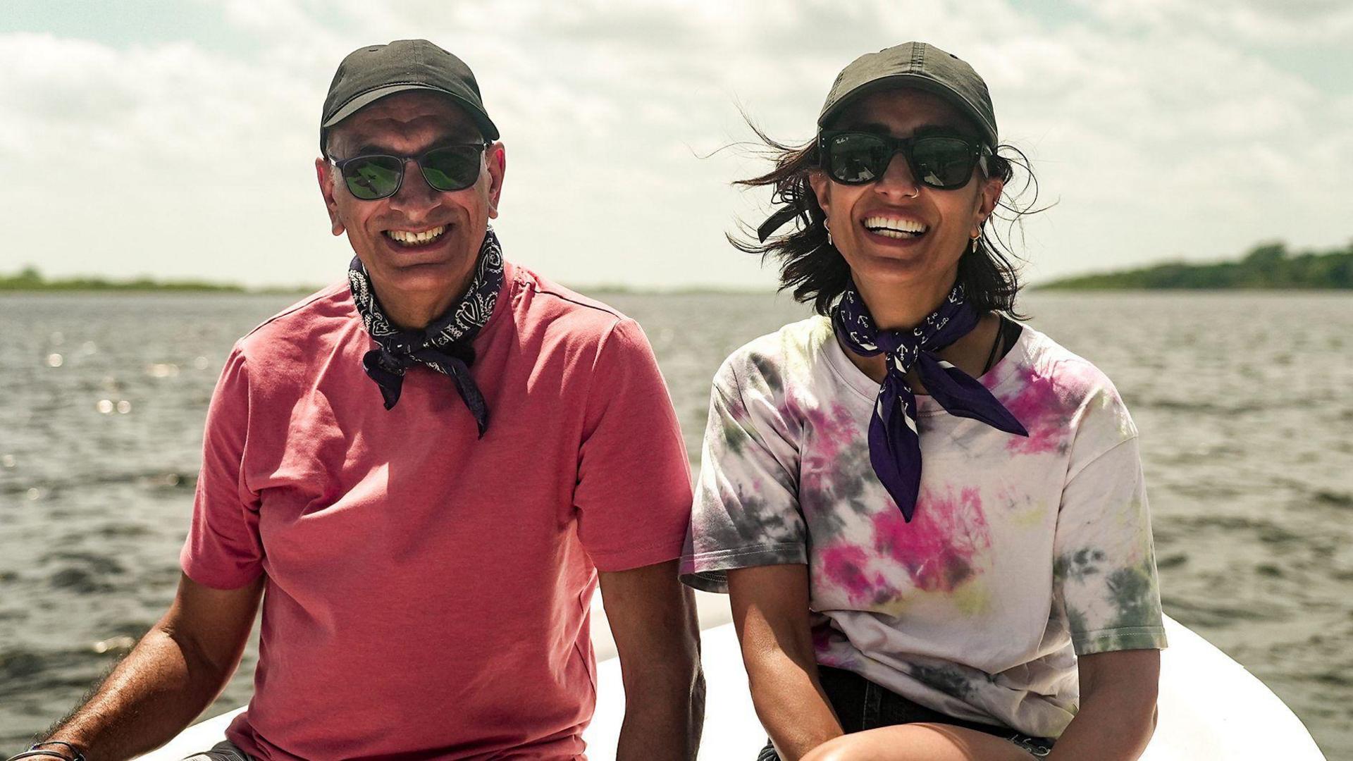 Anita Rani and dad Bal smiling whilst on a boat wearing matching navy neckerchiefs.