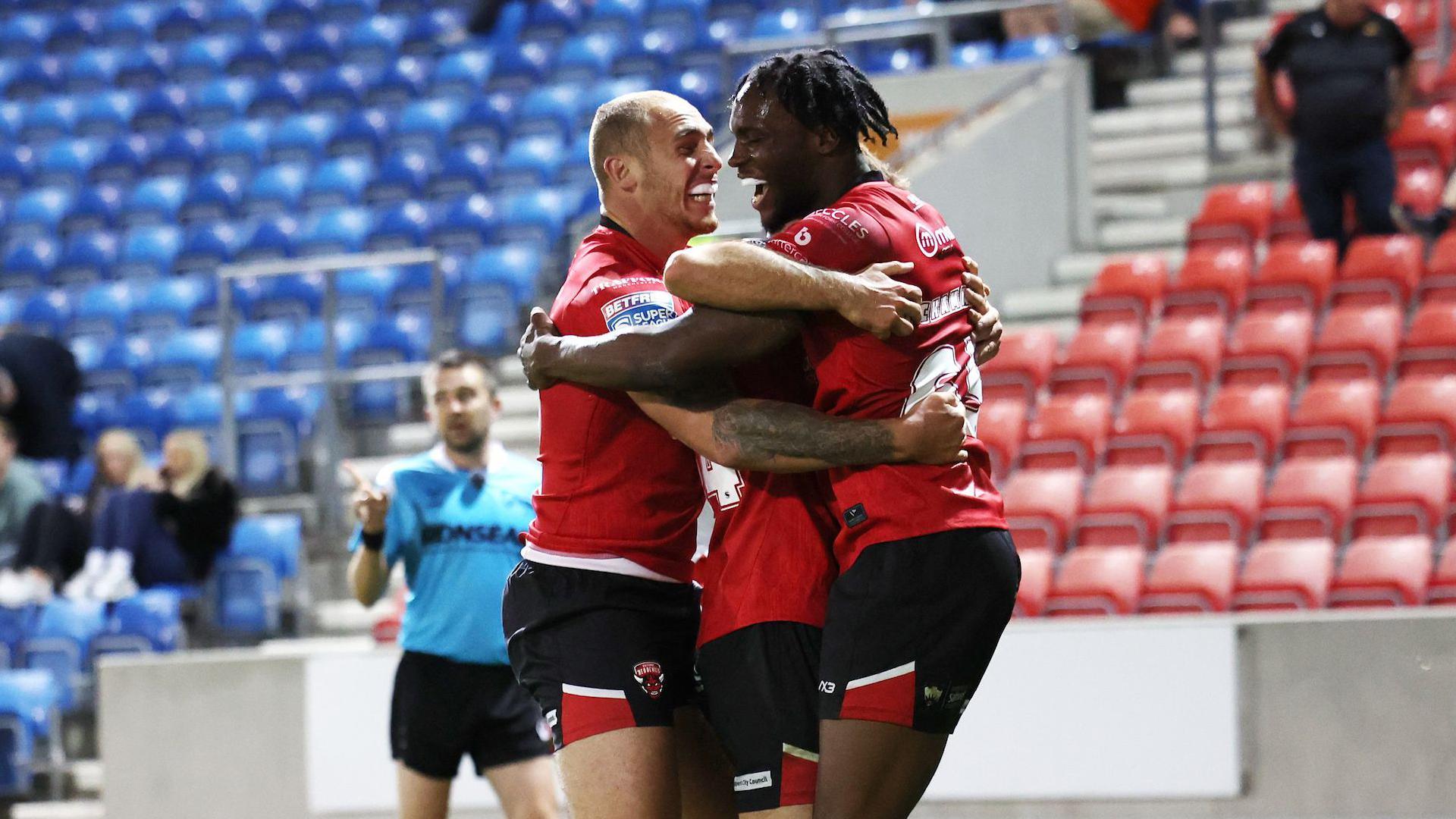 Three Salford Red Devils players celebrate scoring a try during a match in 2025