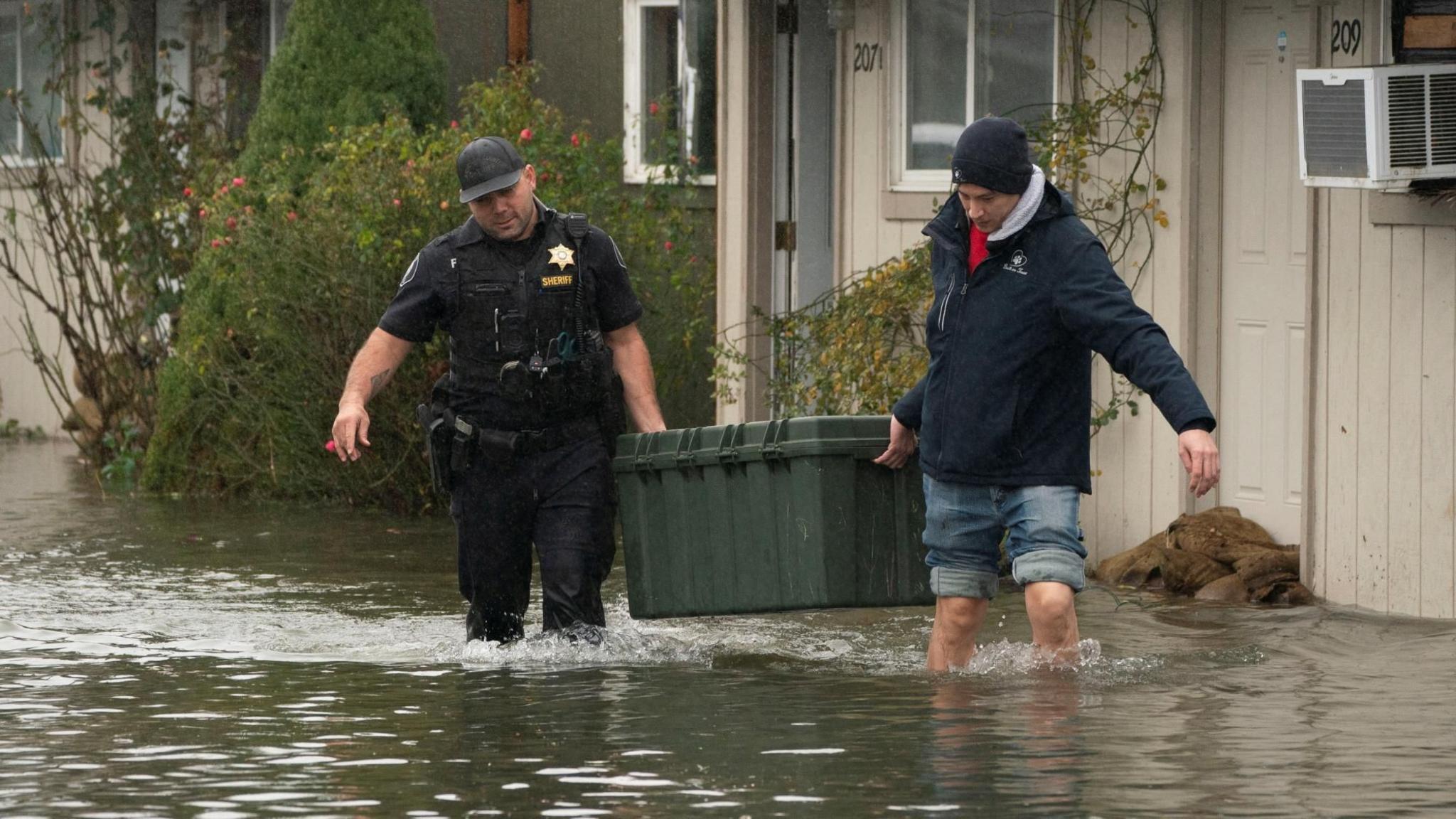 Deputy Sheriff Kalani Apilado helps Brandon Phasith carry belongings while evacuating amidst rising floodwater, as an atmospheric river brings rain and flooding to the Pacific Northwest, in Sultan, Washington