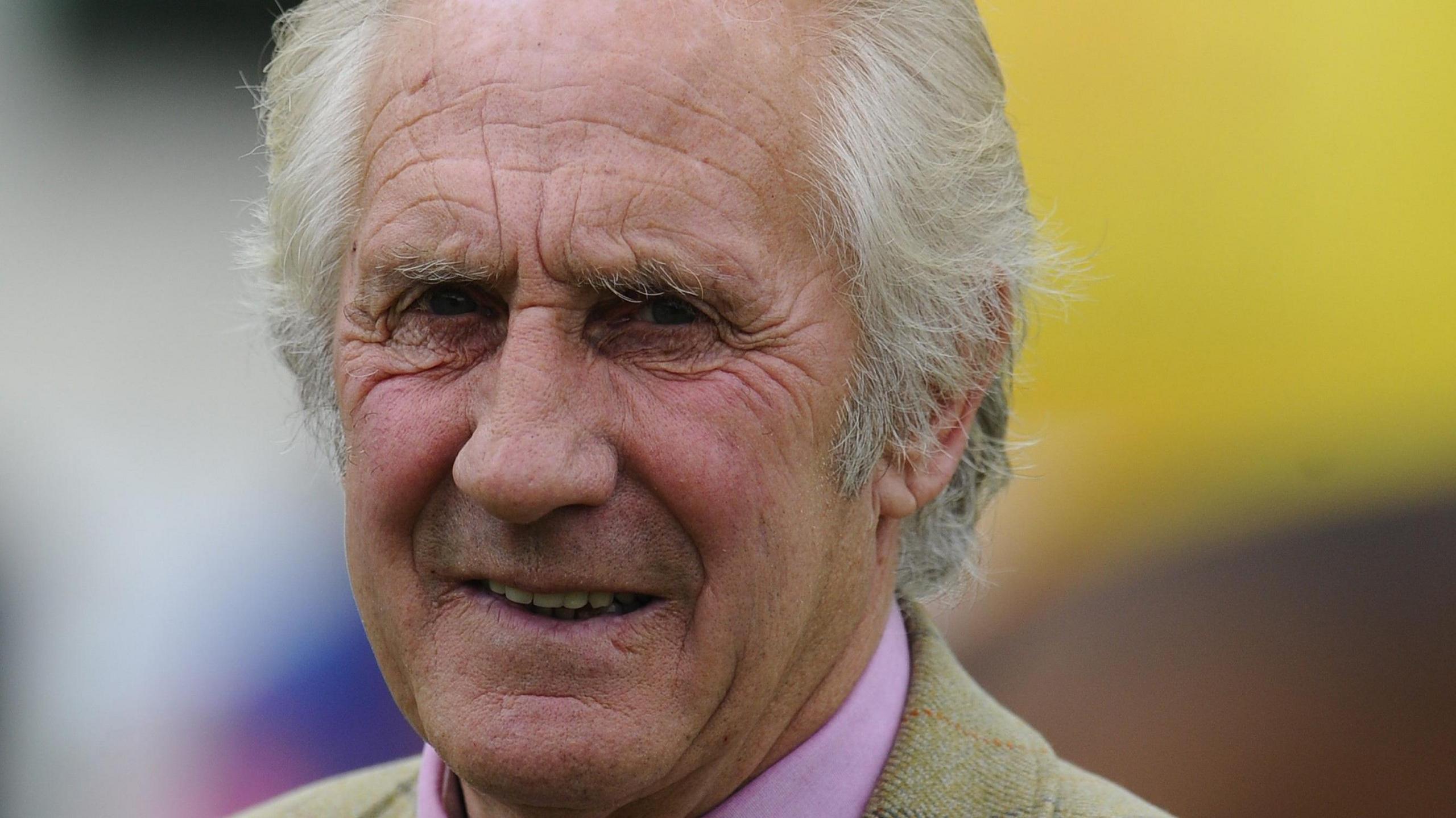 Bill Turner. He is an older man with white short hair. He is squinting and his mouth is open slightly. The collar of his pink shirt is visible and he is wearing a light coloured jacket over the top.