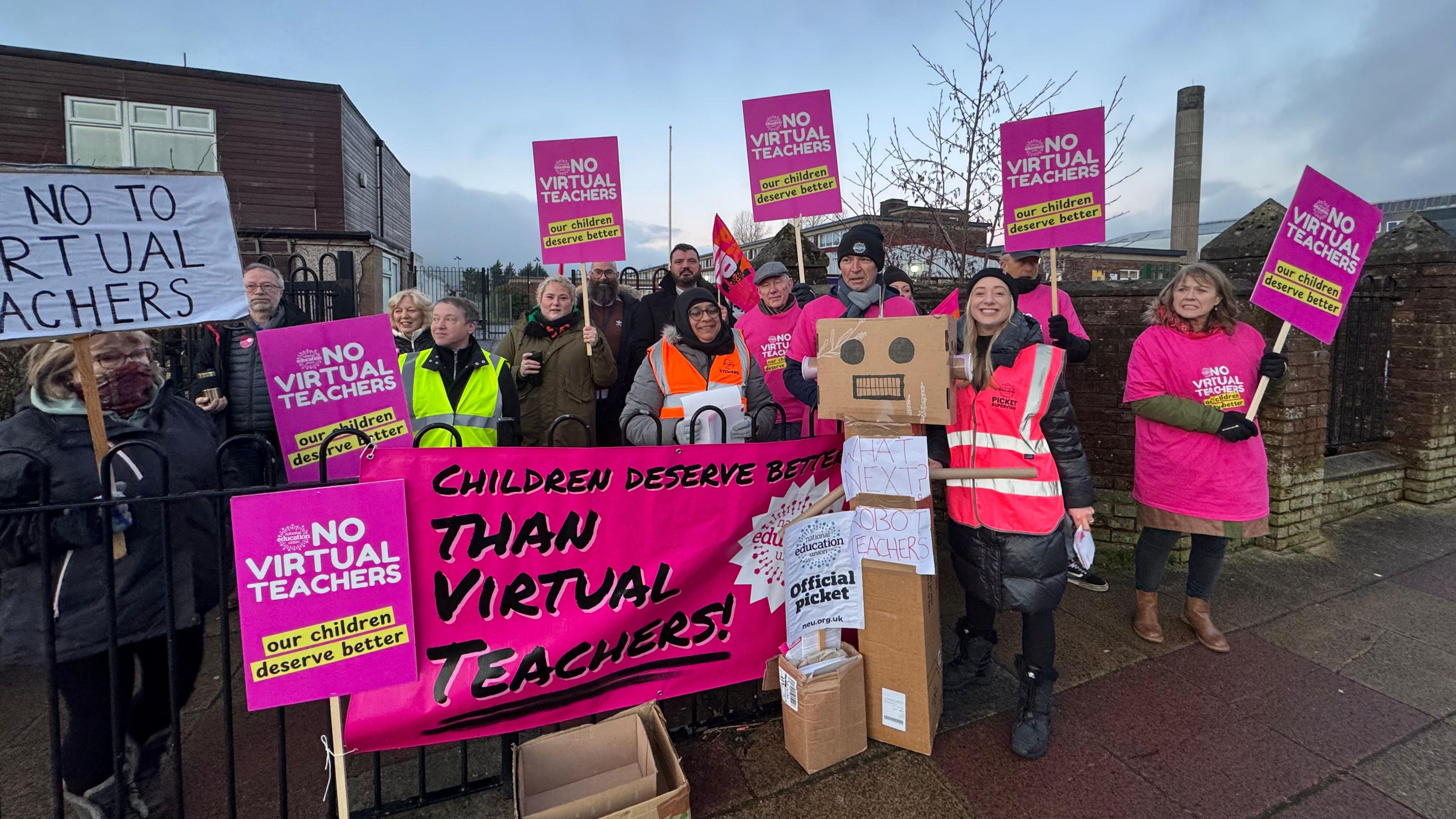 The picket line at teacher strikes in Lancashire, over use of a virtual teacher. Photo shows teachers on the picket line holding NEU signs and banners saying 'no virtual teachers'