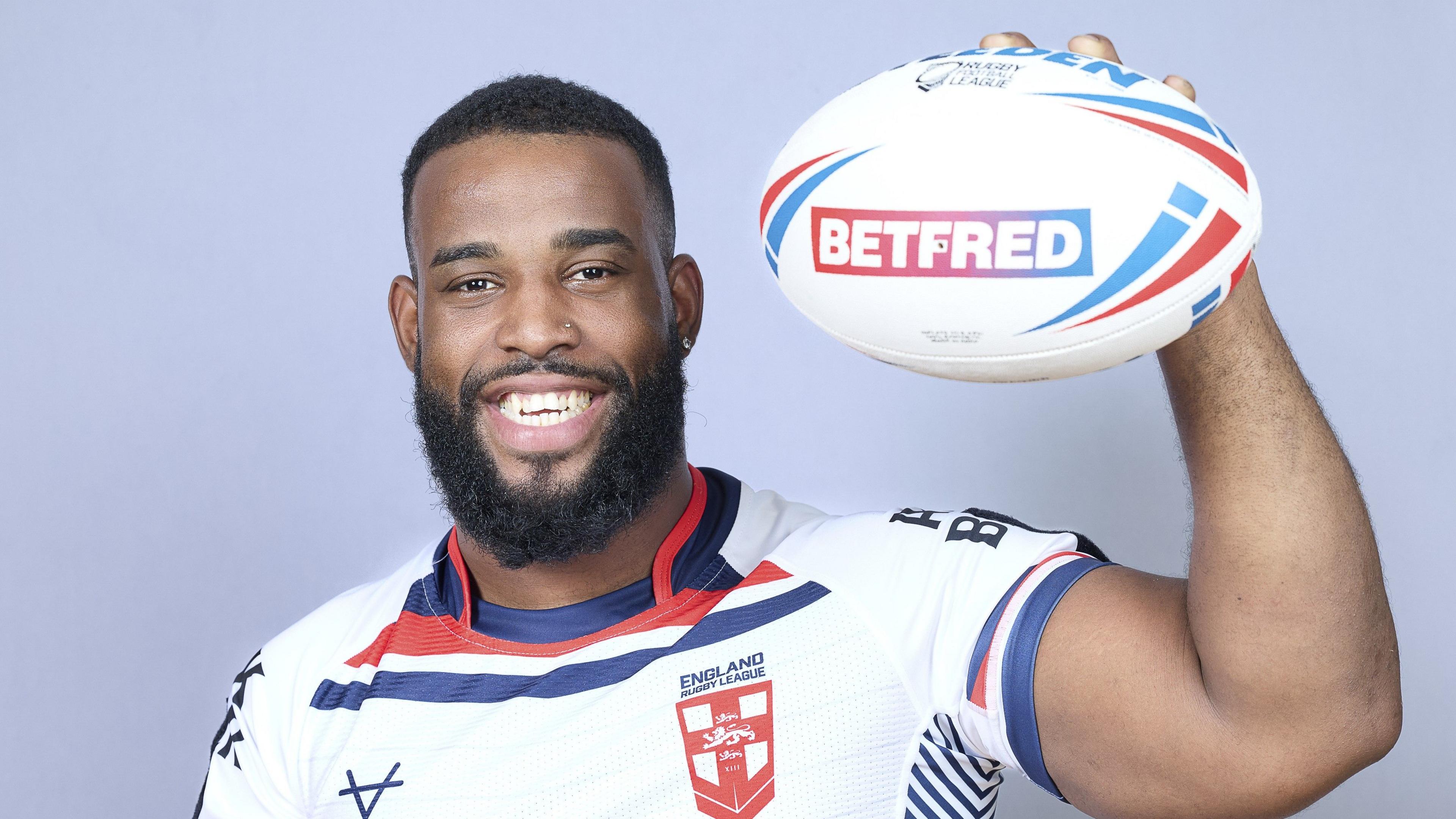 Luis Domingos, wearing an England shirt, grins and holds up the ball for the camera