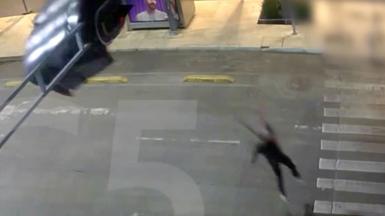 A person wears a parachute, dangling from a traffic light above a road.