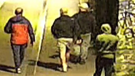 A CCTV image of four men in a street at night time. They are wearing dark clothing. Two are wearing caps, one has a green hoody on and one is bare headed and has a bald patch.