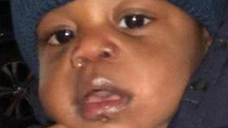 The close up image of a young boy. He is a few months old. He has big brown eyes and wearing a navy coat and navy wool hat.