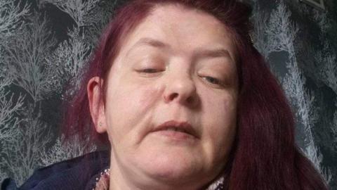 A woman with red hair lies on a grey background looking at the camera