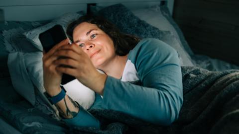 Smiling woman using smartphone in bed at night