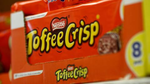 A close-up image of a bright orange box of Nestle Toffee Crisp bars on display in a shop