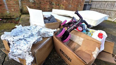 A pile of fly-tipped junk, including a table, two mattresses, a small child's bike, cardboard boxes and foil.