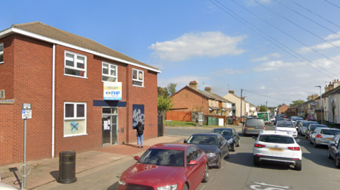 Street view of the vacant building - a red-brick building with cars parked on the street on either side.