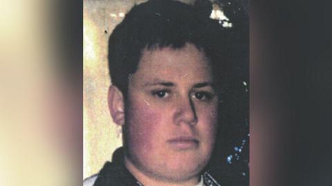 Philip Fudge, who went missing as a 21-year-old, is photographed with short brown hair and brown eyes while wearing a jumper with black collar.