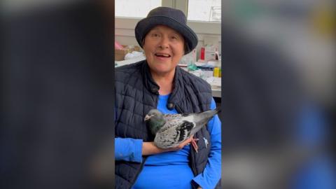 Gudrun Stürmer in a hat and blue top, holding a pigeon