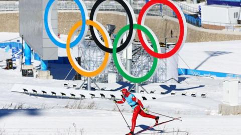 A cross-country skier in front of the Olympic rings