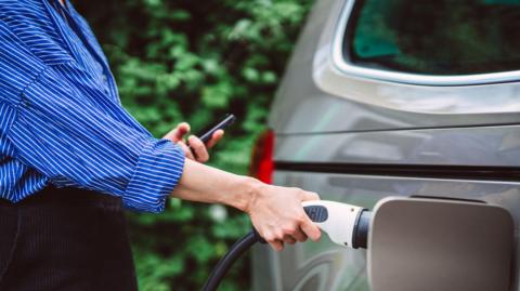 A woman wearing a blue and white striped shirt charges an electric car.