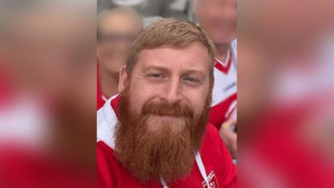 Family photograph of James Adam Barlow. He has red hair and a beard and is wearing a red and white Hull Kingston Rovers top.