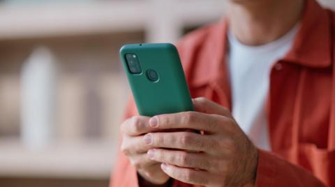 A person wearing a bright, orange jacket and white t-shirt types on a smartphone held in their hands.