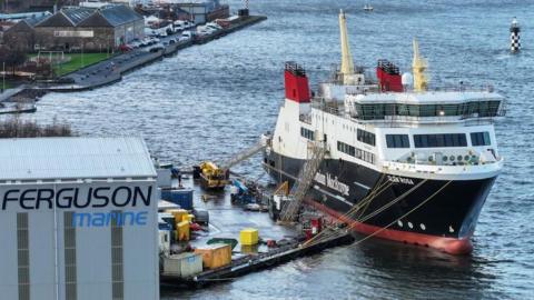 A large red white and black ferry moored beside a large building with Ferguson Marine on the side