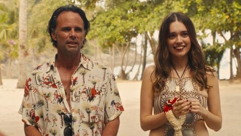 Walton Goggins and Aimee Lou Wood, in costume, stand next to each other on a beach in a scene from the White Lotus