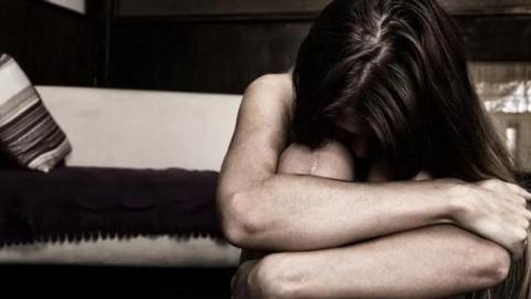 A woman is crouched down and curled up in a ball. She seems scared and upset.