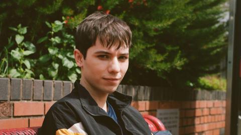 Ellis Howard wears a black zip-up jacket. He has short brown hair and is staring in to the camera.