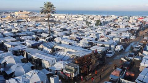White tents packed closely together stand near a seashore on a clear day.