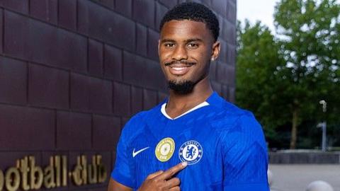 Jorrel Hato points to the Chelsea badge on his shirt after signing