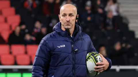 Newcastle Red Bulls head coach Alan Dickens, with a ball under his arm, watching his side warm-up ahead of the game in Lyon