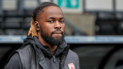 Dynel Simeu with a padded jacket and hoodie on ahead of a match during his loan spell with Morecambe