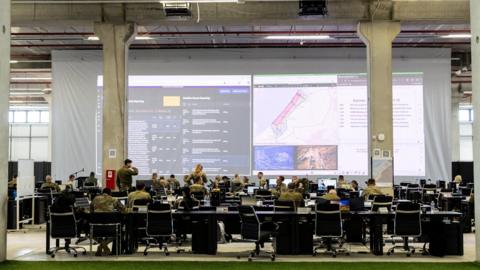 US and other international military personnel work in front of a map of Gaza at the Civil-Military Coordination Centre (CMCC) in Kiryat Gat, southern Israel