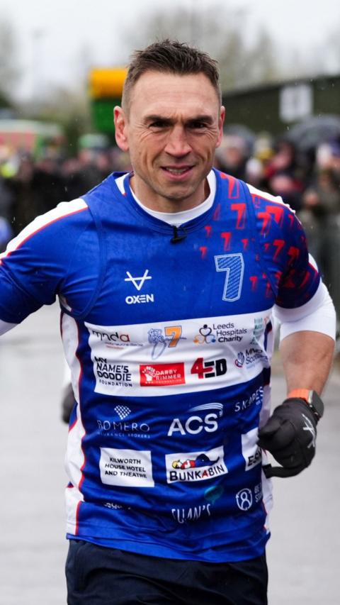 Kevin Sinfield running in a blue shirt with MND charities' logos on it