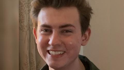 Ethan Scott Brown, young man with dark hair, is looking at the camera and smiling.