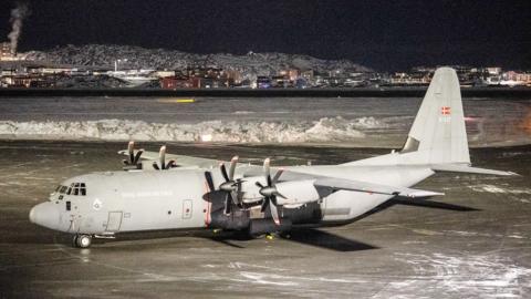 A Royal Danish Air Force Lockheed C-130J Super Hercules aircraft vehicle is parked on the tarmac at Nuuk international airport, Greenland. Snow has been cleared from the tarmac and is piled in an area behind the plane..