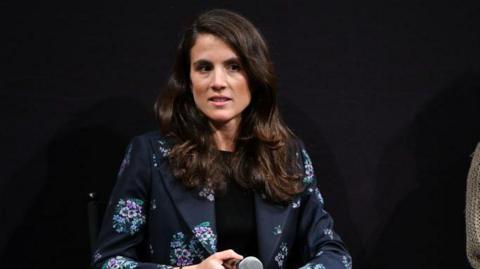 Schlossberg holding a microphone at a speaking event