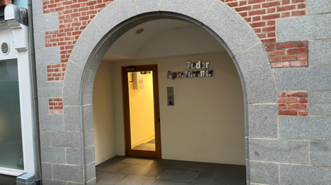The archway entrance of a building with Tudor Apartments to the right of the door inside.