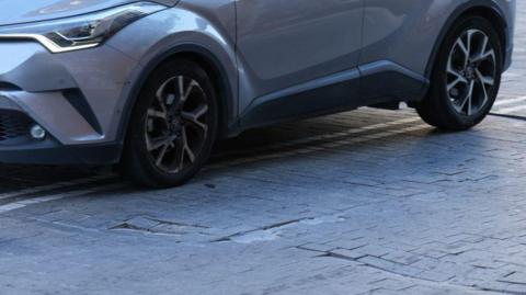 Just the wheels of a silver car can be seen.