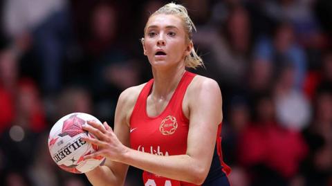 Helen Hounsby holds netball in red England kit.