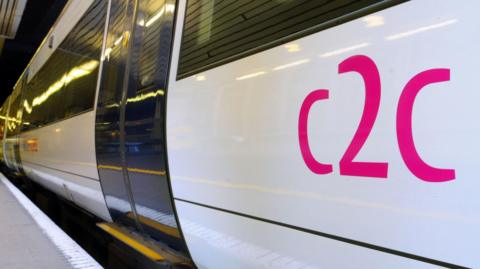 A white train stopped at a platform. It has blue doors and "c2c" printed in pink on the side.