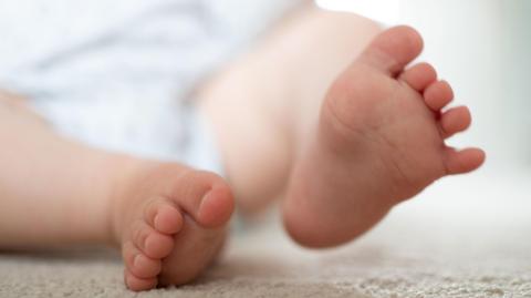 A close of photo of a baby's feet. The baby is lying on a beige carpet with his right foot slightly lifted.
