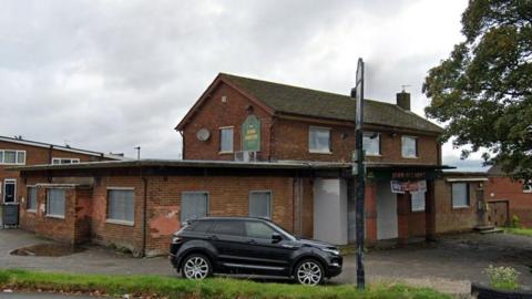 A weathered brick pub named "John O'Gaunt" with boarded-up windows and faded signage, including "John Smith's" and "Sky Sports Live Here".