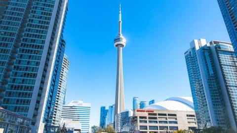 A photograph of the downtown Toronto. The CN Tower stands in the middle, with modern looking skyscrapers all around it.